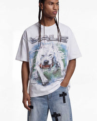 A model wearing a white graphic t-shirt featuring a large print of a white dog and the word 'VALE' in metallic lettering, paired with light blue jeans that have black cross details on the pockets.