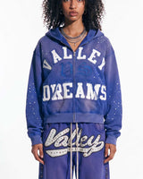 A model wearing a matching purple zip-up hoodie and sweatpants set with 'Valley Dreams' text and rhinestone embellishments, photographed against a plain white background.