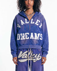 A model wearing a matching purple zip-up hoodie and sweatpants set with 'Valley Dreams' text and rhinestone embellishments, photographed against a plain white background.