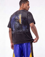 A man wearing a faded black graphic t-shirt with a large 'BOUND BY FATE' print on the back, paired with blue and yellow athletic shorts, photographed against a white studio background.