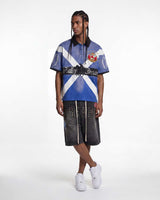 Model wearing Vale Forever Legacy Short Sleeve Polo blue with studded pants, full front view