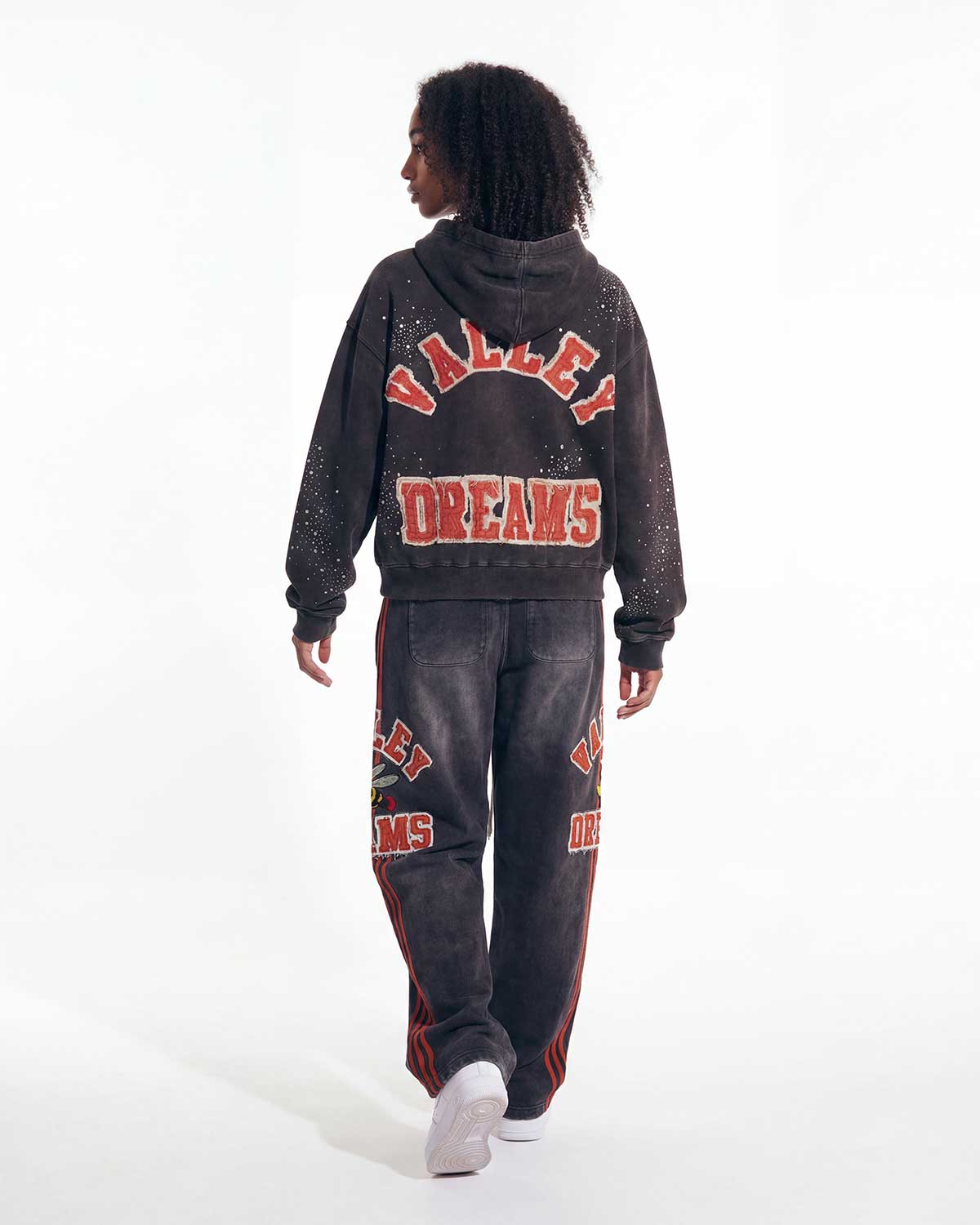 A model shown from the back wearing a matching washed black hoodie and sweatpants set with red and white 'VALLEY DREAMS' text graphics, set against a plain white studio background.
