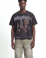 A man wearing a faded black graphic t-shirt with a horror movie print and light beige cargo pants, standing against a white studio background.