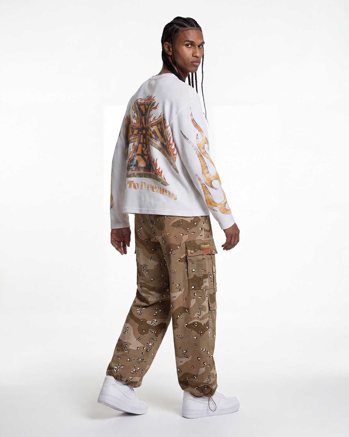 A model shown from the back wearing a white long-sleeve sweatshirt with a large gold and brown graphic print on the back, paired with brown camouflage cargo pants and white sneakers, against a plain white studio background.