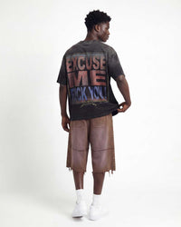 A man shown from the back wearing a dark gray graphic t-shirt with a distressed 'EXCUSE ME F*CK YOU!' print, brown frayed mid-calf shorts, white socks, and white sneakers, against a plain white studio background.