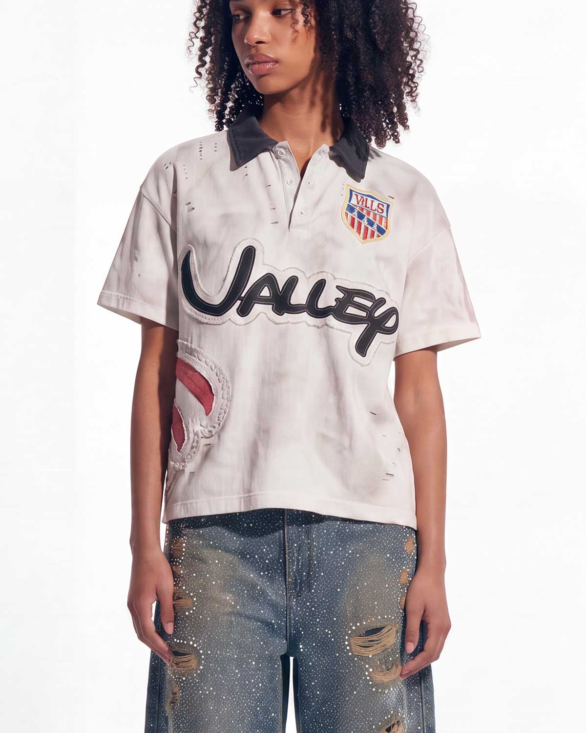 A model wearing a distressed white short-sleeve polo shirt with a dark gray collar, a large black 'UNISEX' logo across the front, a colorful crest on the left chest, and a distressed blue jeans.
