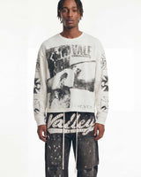 A model wearing a white long-sleeve crewneck sweatshirt with a large black and white graphic print on the front and 'Valley' text on the sleeves, paired with dark distressed pants against a plain white background.
