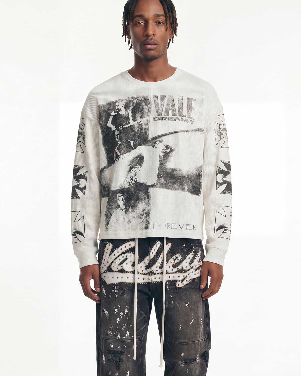 A model wearing a white long-sleeve crewneck sweatshirt with a large black and white graphic print on the front and 'Valley' text on the sleeves, paired with dark distressed pants against a plain white background.