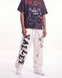 A person modeling an oversized faded black graphic T-shirt and off-white distressed sweatpants with large black 'VALLEY' lettering down one leg, paired with white sneakers against a plain white studio background.