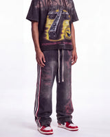 A person wearing a dark graphic T-shirt and matching dark gray washed sweatpants with white drawstrings and red/white side stripes, paired with red and white sneakers, against a plain white studio background.