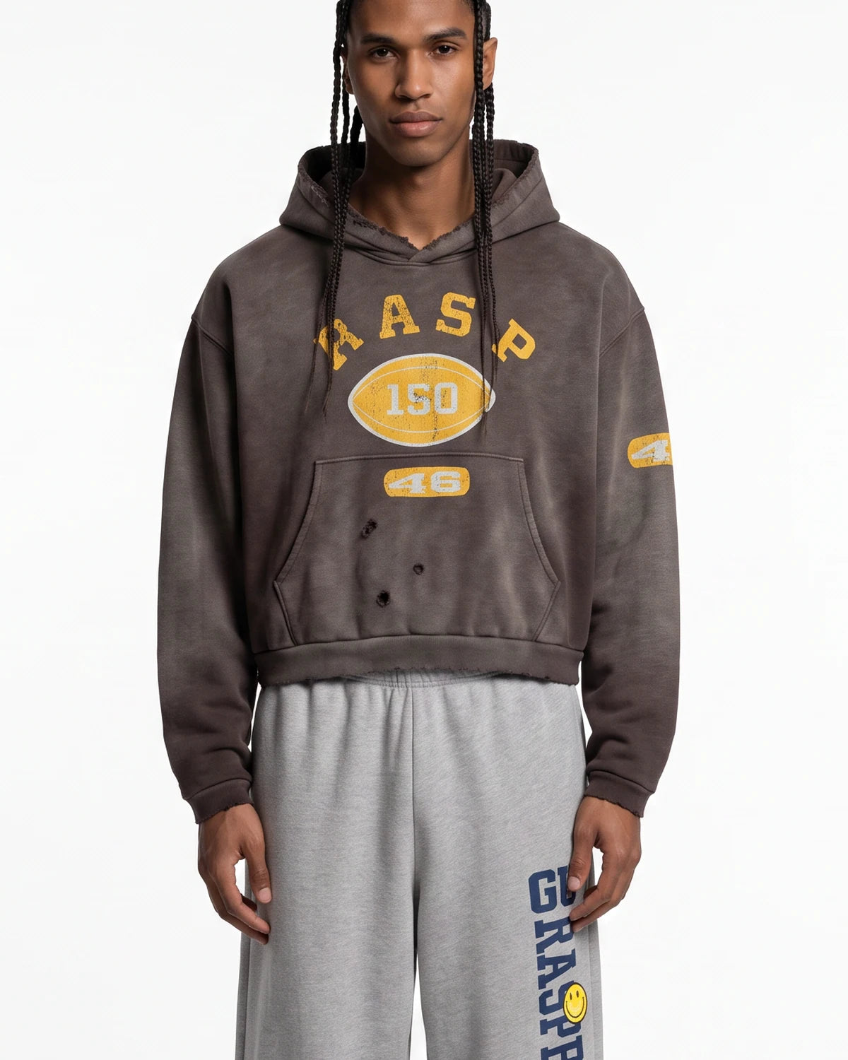 A model wearing a dark brown washed cropped hoodie with yellow varsity-style graphics reading 'RASP 150' and '46', paired with light gray sweatpants, against a plain white background.