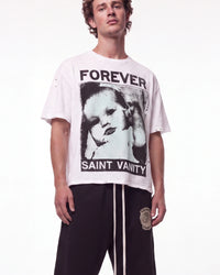 A male model wearing a white Saint Vanity graphic t-shirt with a black-and-white portrait print and distressed details, paired with black sweatpants, against a plain white studio background.