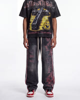 A person wearing a black graphic t-shirt and matching black distressed sweatpants with red and white side stripes and vertical lettering, paired with red and white sneakers, against a plain white studio background.