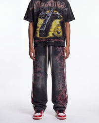 A person wearing a black graphic t-shirt and matching black distressed sweatpants with red and white side stripes and vertical lettering, paired with red and white sneakers, against a plain white studio background.