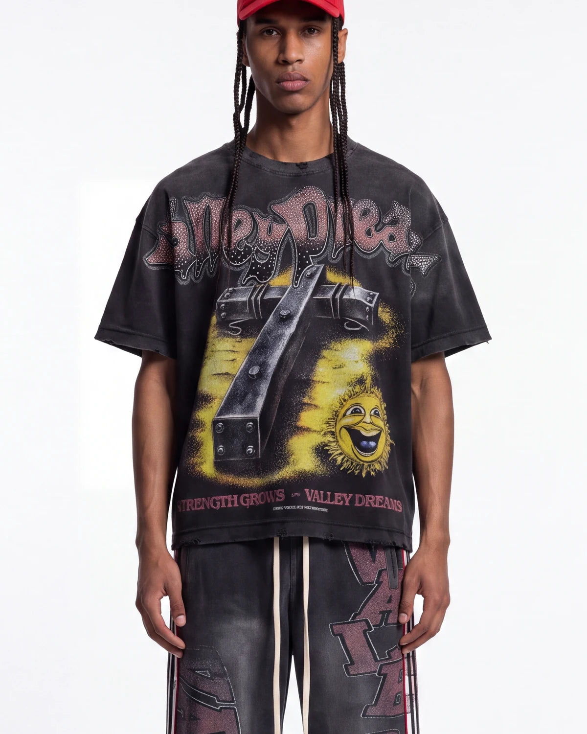 A model wearing a black acid-washed Grunt Style t-shirt with a large yellow and black graphic print, paired with matching acid-washed pants and a red cap, against a plain white background.