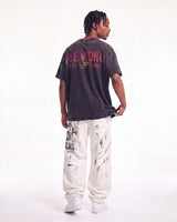 A man shown from the back wearing a faded black graphic t-shirt with 'FLE WORLD' printed in red and yellow, paired with white sweatpants and white sneakers, against a plain white studio background.