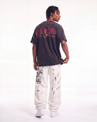 A man shown from the back wearing a faded black graphic t-shirt with 'FLE WORLD' printed in red and yellow, paired with white sweatpants and white sneakers, against a plain white studio background.
