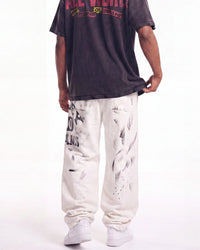 A person shown from the back wearing a faded black graphic t-shirt, off-white sweatpants with black paint splatter graphics, and white sneakers against a plain white background.