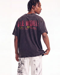 A man shown from the back wearing a faded black graphic t-shirt with 'ALL WORLD OF DISCIPLINE' printed in red and yellow on the back, paired with white distressed pants, against a plain white background.