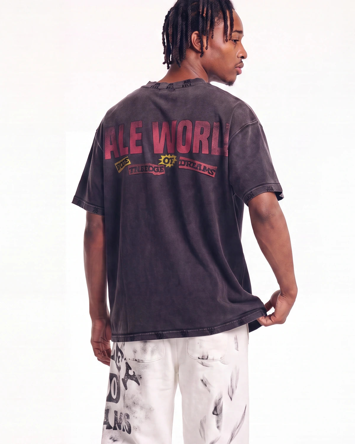 A man shown from the back wearing a faded black graphic t-shirt with 'ALL WORLD OF DISCIPLINE' printed in red and yellow on the back, paired with white distressed pants, against a plain white background.